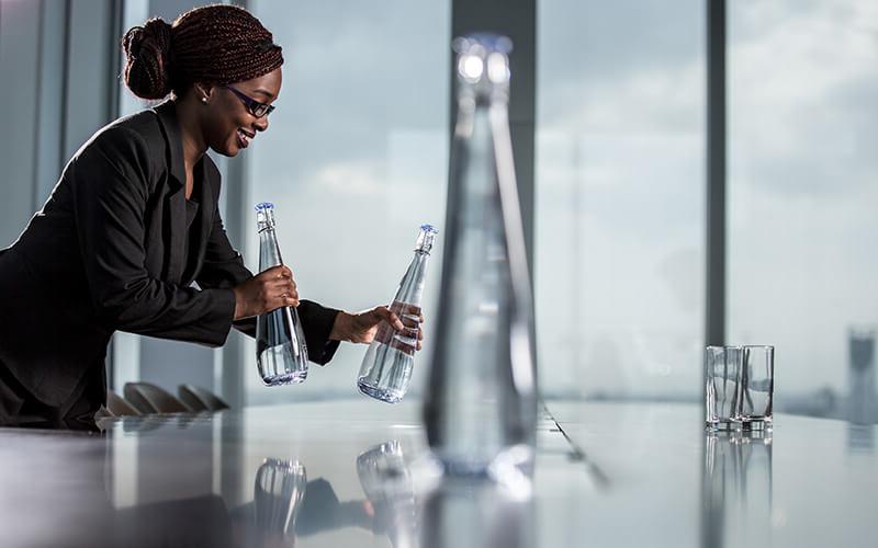Woman placing glass water bottles on an office meeting table
